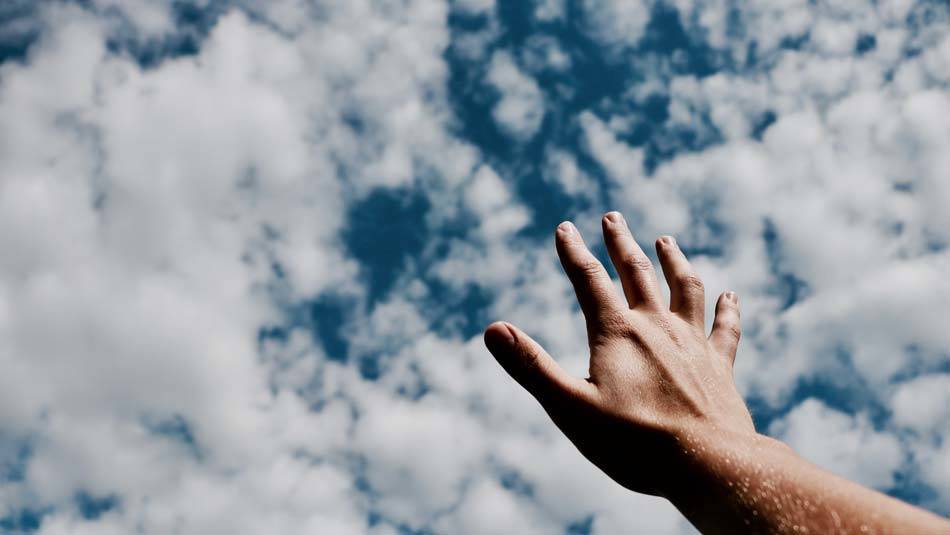 Hand stretched wit open palm towards the sky filled with white clouds, reaching out to God in hope and faith - AAAF