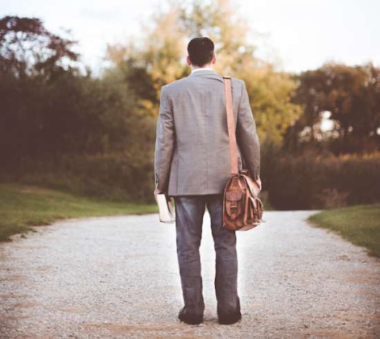 A man standing on a pathway with a messenger bag over one arm and a Bible in his hand