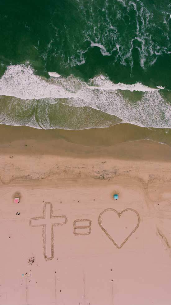 Cross equals Love drawn on sand at the beach, as we are drawn back in love to God through His Son Jesus Christ