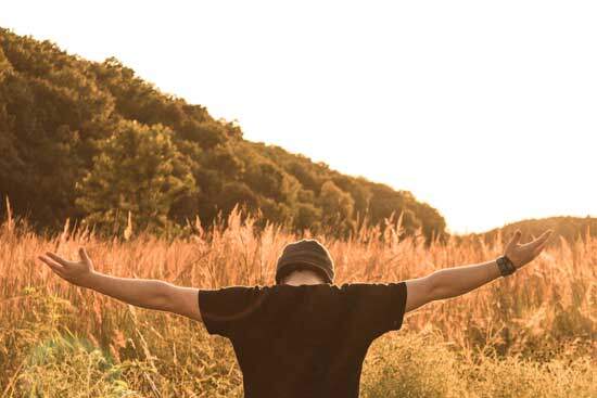 Man with his arms stretched out in an open field, surrendering His life to God, under the conviction of the Holy Spirit