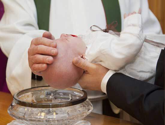 A priest sprinkling water on a baby's head during infant baptism
