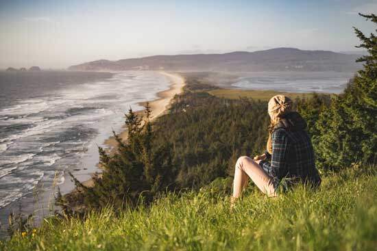 A woman sitting on a grassy hillside that overlooks the ocean and spending time with God in nature