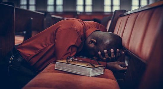 Man with head down praying in a church pew after sermon finished.