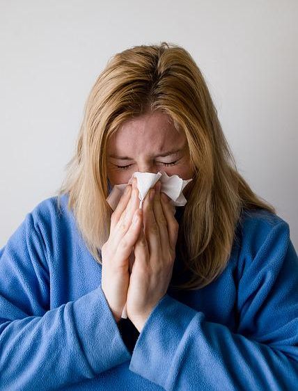 A woman blowing her nose because her immune system is weakened from lack of sleep