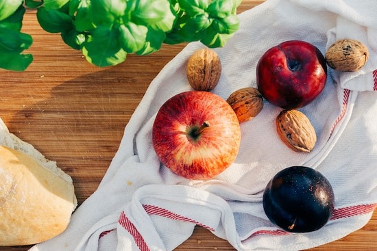 An assortment of plant foods on a cloth: apple, plum, nuts, bread, and basil