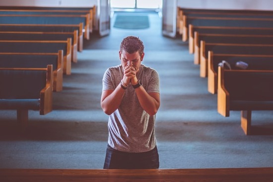 A Christian man kneels at the front of a church to pray