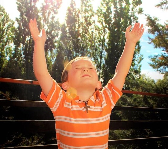 A child looking up and lifting hands up in prayer