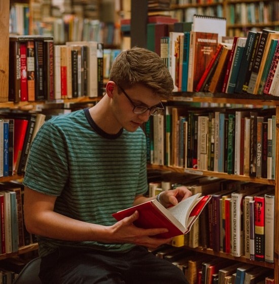 A young man sitting in a library and opening up a book