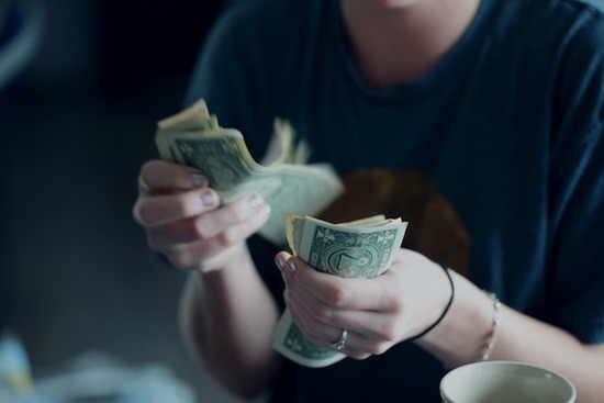 A young woman counting dollar bills to try to pay her debt