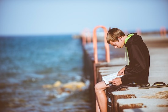 A teenage boy sitting on a dock and reading the Bible