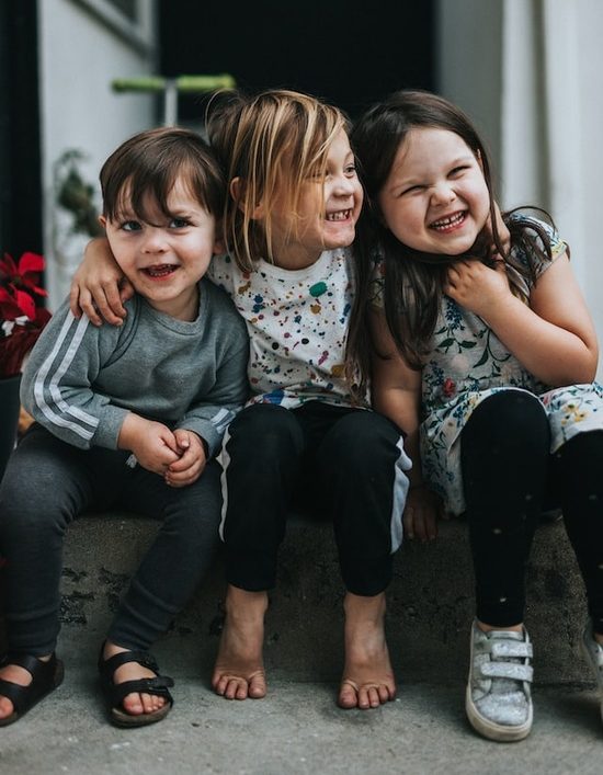 Three children with their arms around each other, laughing, to represent the delight and joy that Jesus wants us to have