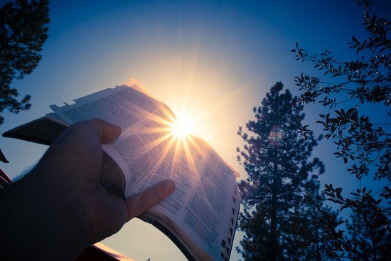 A hand holding a Bible with the sun shining behind