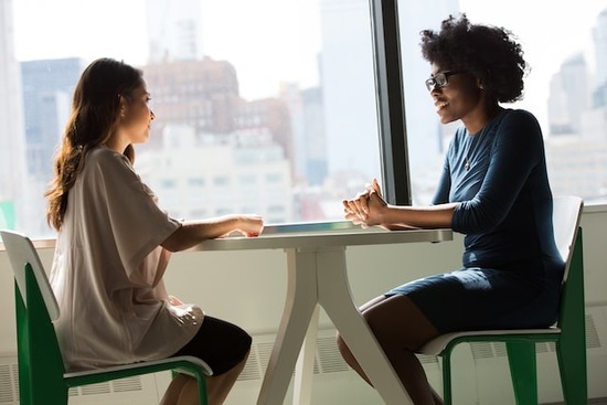 Two women sitting across from each other at a table, illustrating the importance of communication in a relationship just like prayer is our communication with God