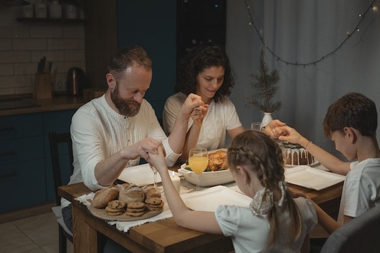 An Adventist family holding hands as they pray over a meal