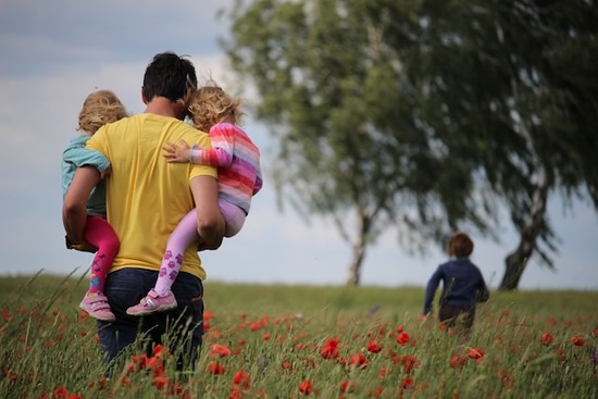 A man carrying two children through a field, representative of the first two children J. N. Andrews had