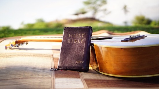 A Bible leaning against a guitar on a picnic blanket
