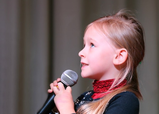 A little girl holding a microphone and using her voice to sing for God