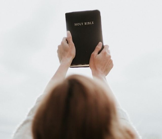 A woman clutching a Bible with both hands and lifting it up