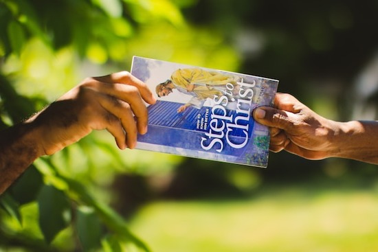 A hand giving Ellen White's book Steps to Christ to someone