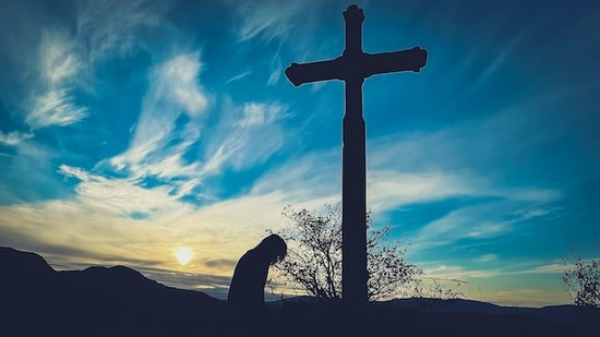 A person kneeling at a cross at twilight