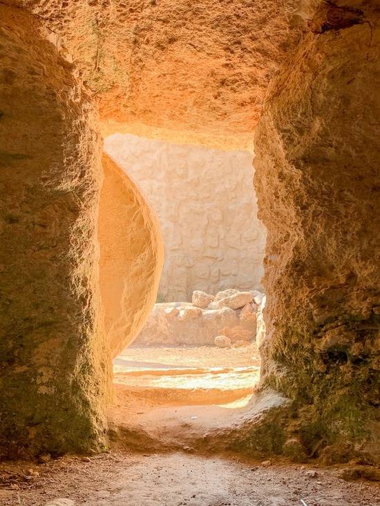 A stone door is rolled away from the entrance of the tomb, flooding the inside of the tomb with light.
