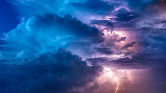 Lightning among clouds, creating a blue and pink sky