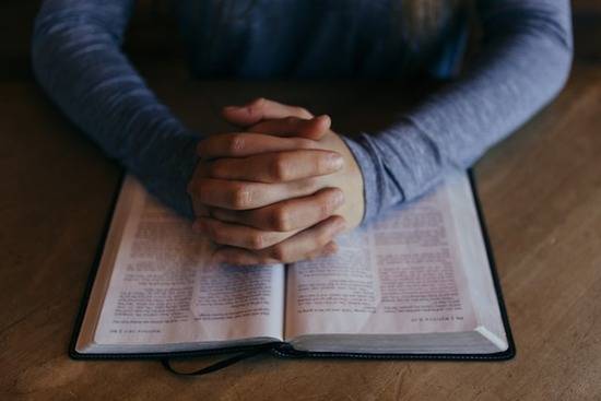  Hands folded in prayer on top of a Bible