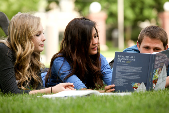 Adventist students laying on the lawn and studying a textbook