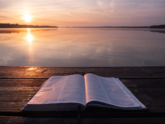 A Bible on a dock overlooking a lake at sunset