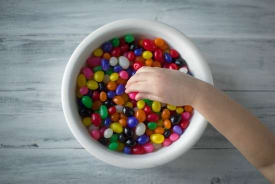 A child's hand reaching into a bowl of jelly beans