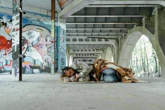 A homeless man sleeping on the ground under a bridge
