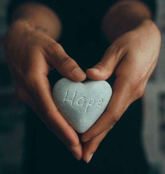 Hands holding a heart-shaped rock with the word Hope etched into it