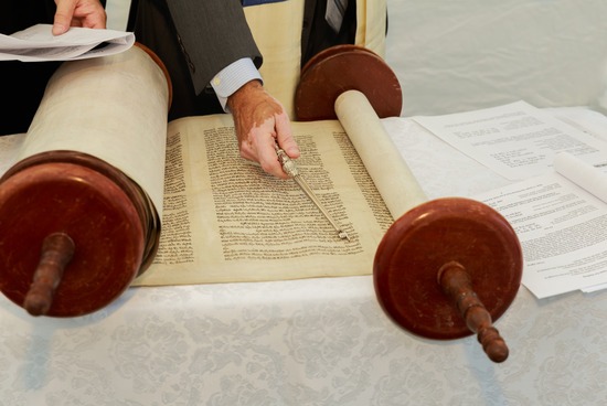 A hand using a pointer to read ancient scrolls of the Bible