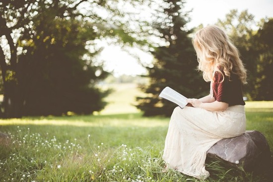  A woman with a necklace sitting in a grassy field and reading her Bible 
