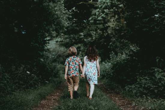 A boy and a girl walk outdoors under a canopy of trees