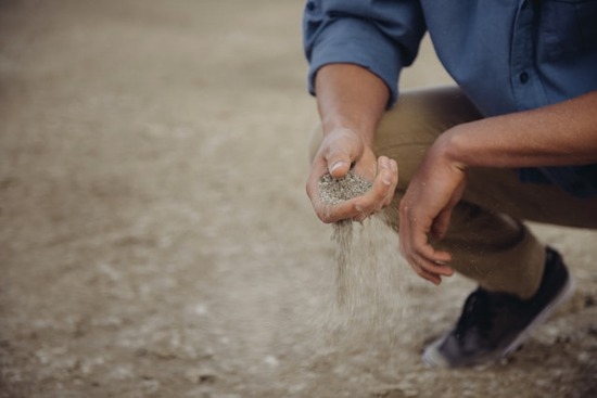 A man crouching down and sifting dirt through his hands