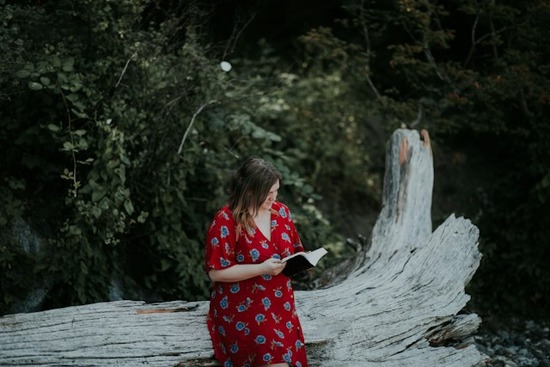 A woman outdoors sitting on a log and reading her Bible with sun exposure
