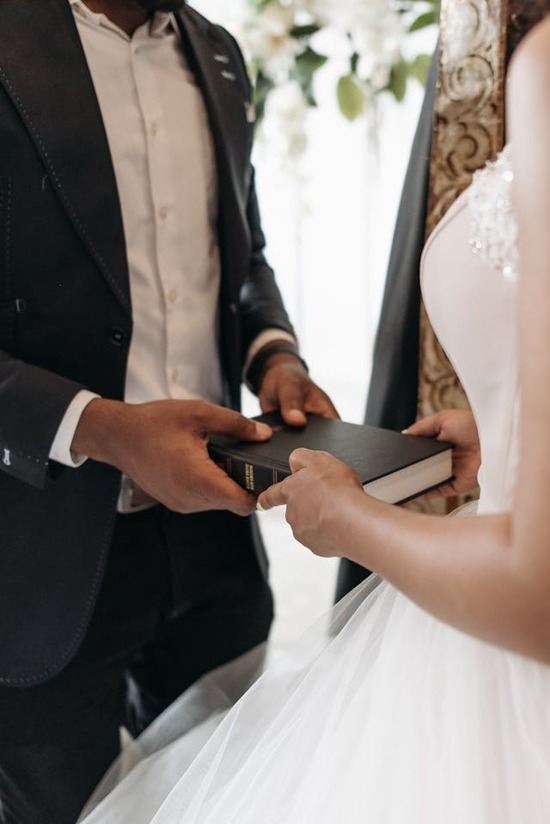A bride and groom facing each other and holding onto a Bible that's between them 