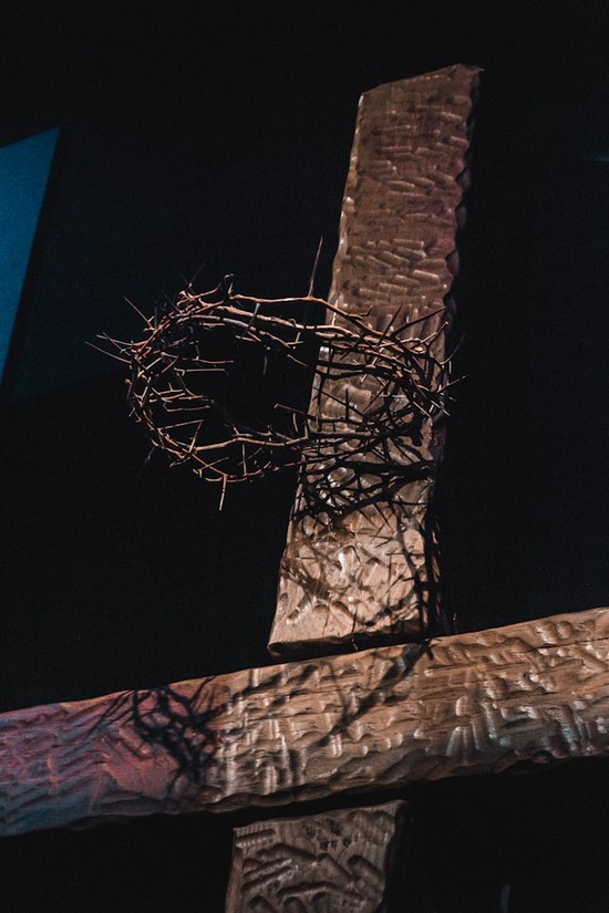 A wooden cross stands as a crown of thorns hangs suspended at the top of the cross where Jesus' head would have been.