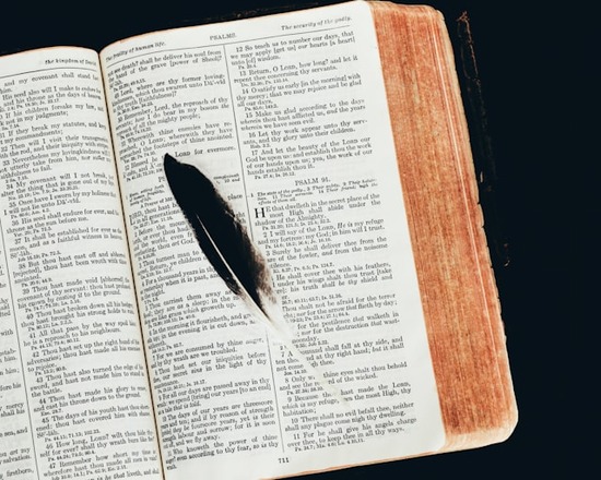 An open Bible with a feather quill resting on its pages.