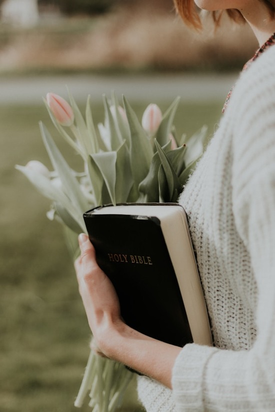 A woman holds a Bible and a bouquet of tulips close.
