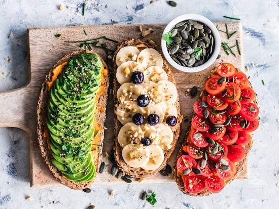 A healthy meal consisting of toasts with different toppings including avocado, tomatoes, and bananas.