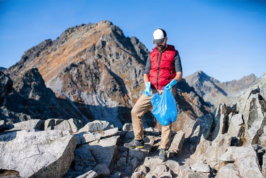 A man with a bag, picking up garbage on a mountain trail 