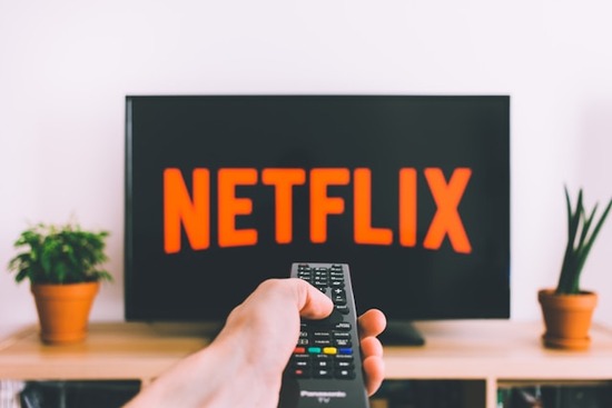 A hand pointing a T.V. remote at a T.V. screen to pull up the latest Netflix shows.