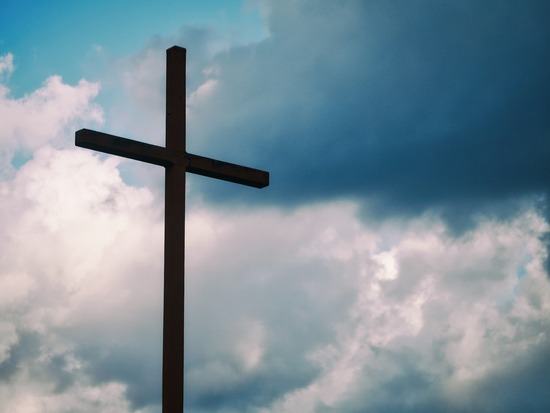 The silhouette of a cross against a cloudy sky.