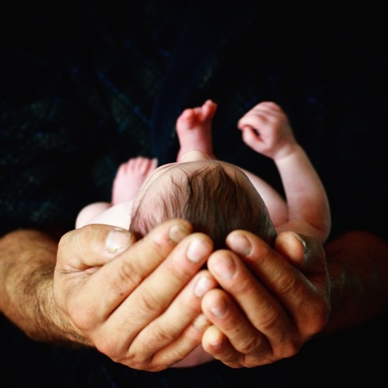 An infant child resting in their parent's hands.