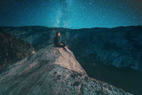 A man on top of a bare mountain, peering into the night sky, looking for Jesus