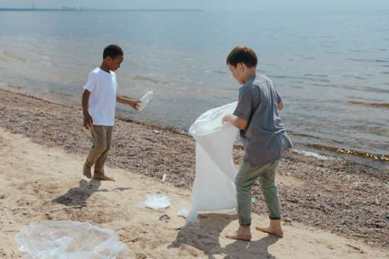 Two boys picking up litter at a beach, which is showing stewardship for our earth