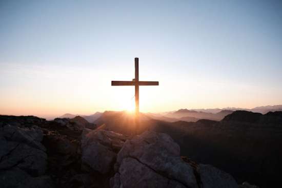 A wooden cross on a mountain with sunlight shining from behind it