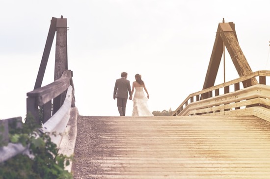 A bride and groom walking together across a bridge 